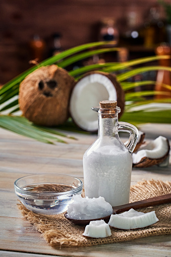 Glass bottle of coconut oil and fresh coconut fruit on wooden rustic white background, alternative therapy medicine concept