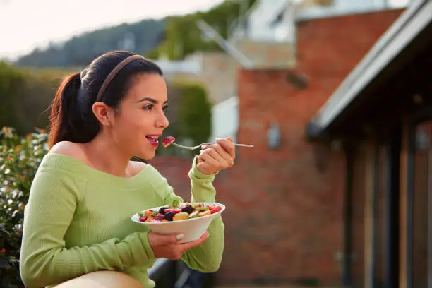 Vegan food themes. Close-up of a Hispanic cute young woman eating fruit salad at lunch outdoors with copy space.