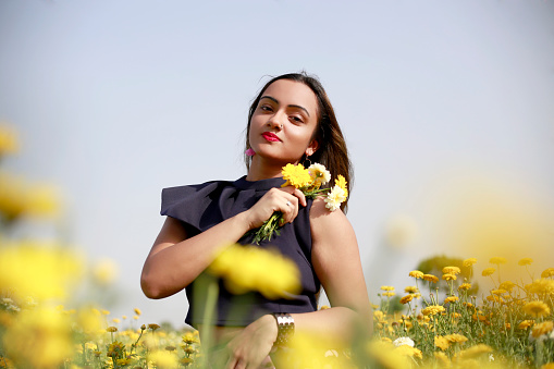 Young girl of Indian ethnicity standing in flower field and she holding yellow flowers in hand.