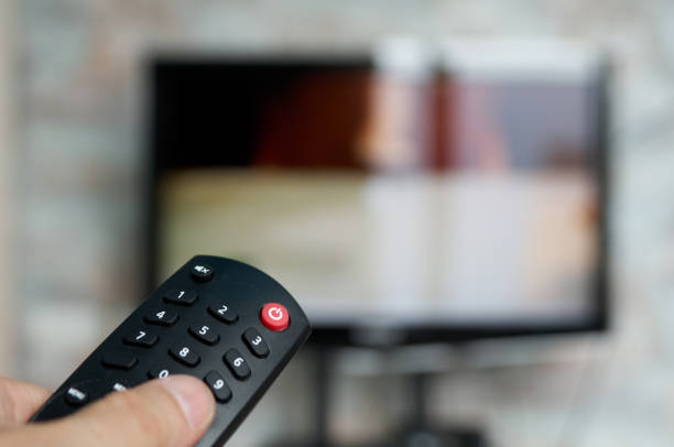 istock Changing TV program: close up of human hand holding television remote control on blured background with TV screen 1415519236