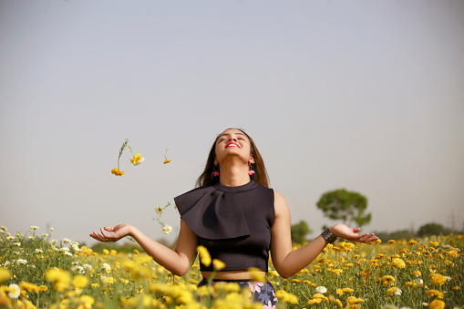 Young teenage girl of Indian ethnicity standing in yellow flowers and she enjoying fresh air.