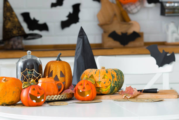 istock Happy Halloween! Pumpkin Jack on the table. Lantern with a carved smile and different attributes of the holiday on a light background in the interior. For family holidays at home. Copyspace. 1415525088