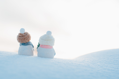 christmas card. Statuette figurine of two snowmen beanie on a snowy background outdoors. Festive decor, warm sunny sunset.