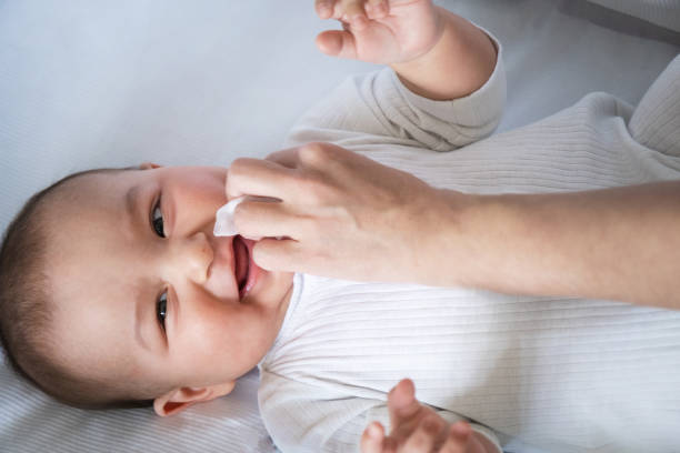Mom wipes the baby's drool with a napkin. Baby care, teething, drooling. stock photo