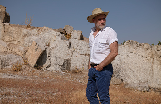 Adult man in cowboy hat and shirt in rock field.
