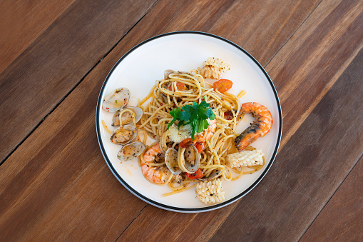 Seafood spaghetti with clams, prawns and cuttlefish in white plate on wooden table.