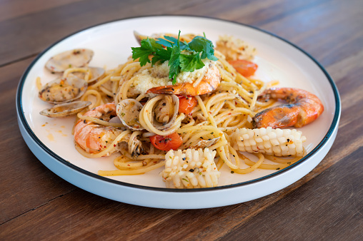 Seafood spaghetti with clams, prawns and cuttlefish in white plate on wooden table.