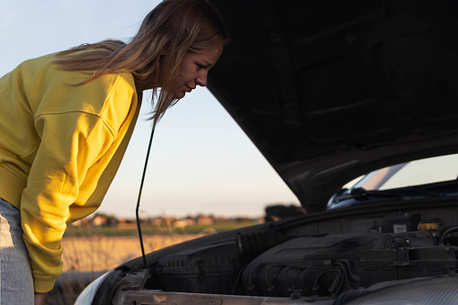 girl stands with the hood of the car open and looks with a surprised look at what has broken holding her head with her hand.there is a place for an inscription on the right. High quality photo