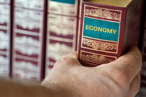 A hand reaching for a book titled Economy, Concept of science and economic knowledge acquisition