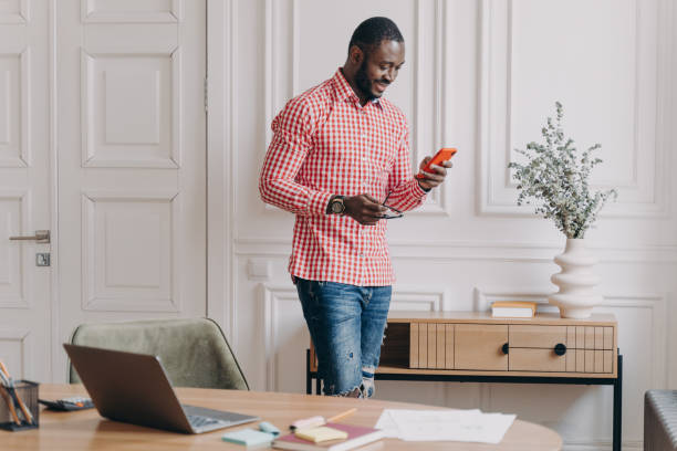 istock Confident handsome african american businessman using mobile, standing in office during working day 1415531884