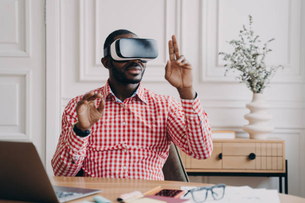 istock Focused Aframerican man in VR glasses enjoying augmented reality while sitting at workplace 1415531888