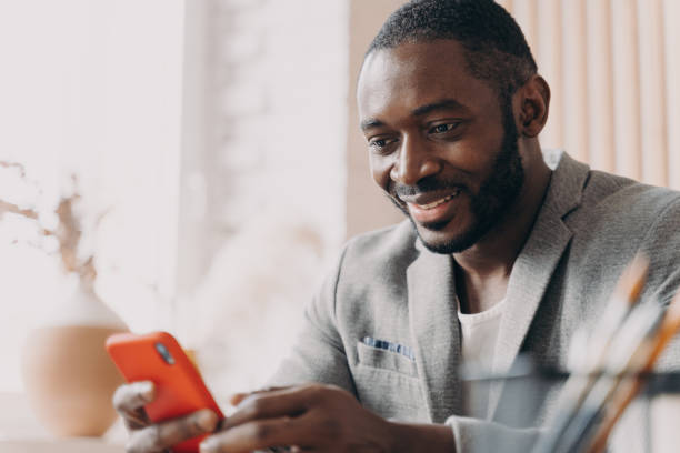 istock Smiling african american businessman using mobile, chatting online while sitting at office desk 1415531905