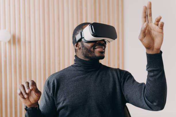 istock Smiling african american businessman in VR glasses sits in office, testing virtual reality goggles 1415531920