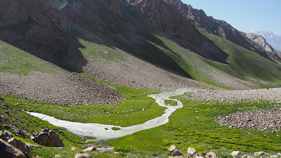 A view from above on a mountain river flowing through a green valley in the Pamir-Alay region, Tajikistan