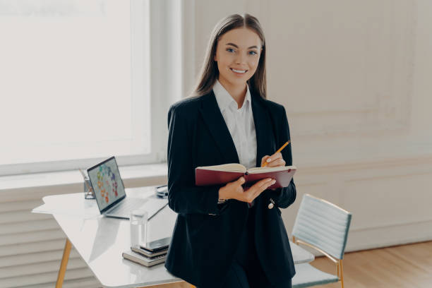 istock Female director holding notebook and pencil while leaning on office desk 1415537637