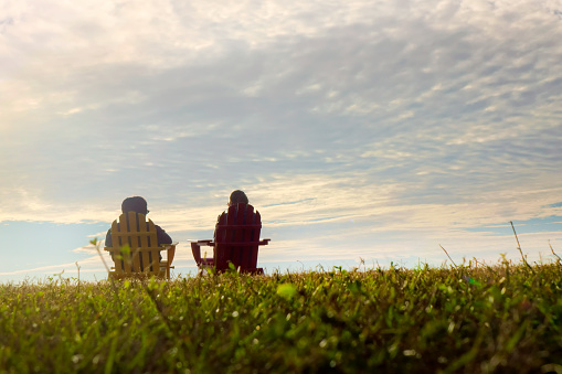 Rear view of two women sitting on Adirondack Chairs and watching seascape