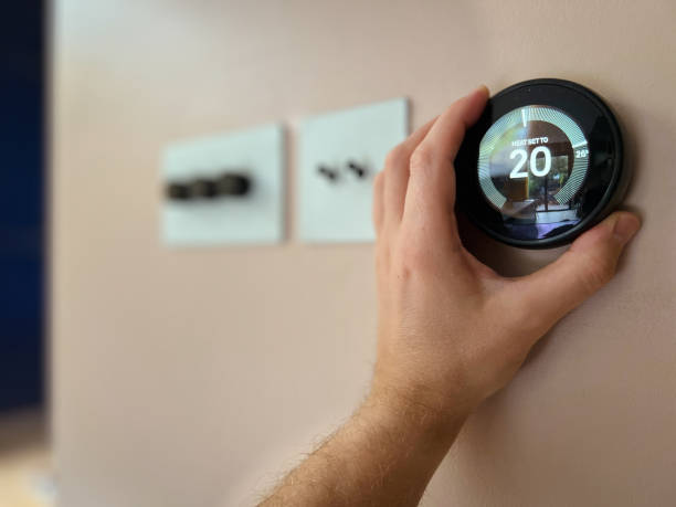 Regulating heating temperature with a modern smart thermostat Man regulating heating temperature with a modern wireless thermostat installed on the wall at home. smart thermostat stock pictures, royalty-free photos & images