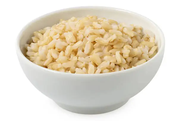 Brown cooked rice in a white ceramic bowl isolated on white.
