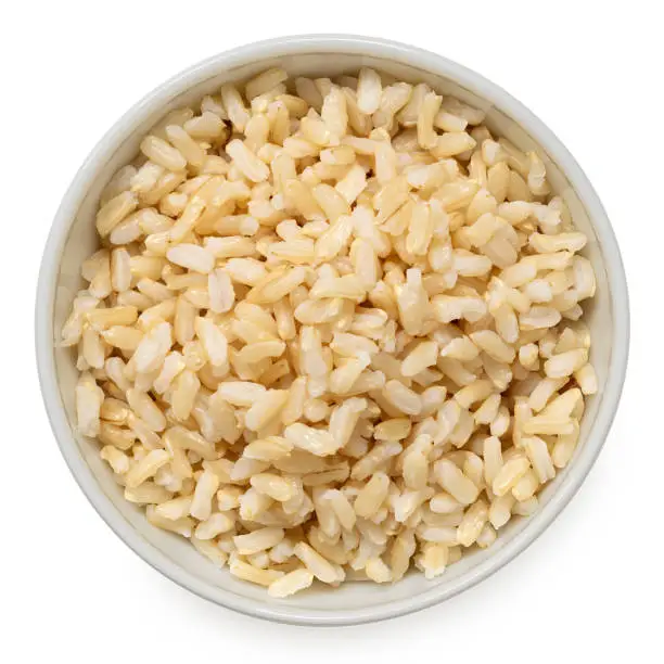 Brown cooked rice in a white ceramic bowl isolated on white. Top view.