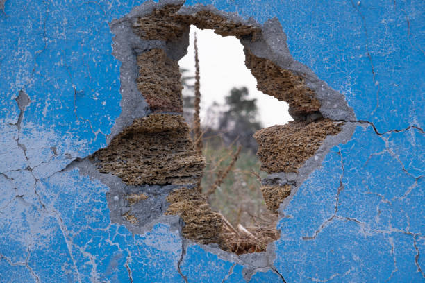 istock Hole in the old wall. Blue textured plaster and shell brick. Through the hole you can see the forest and trees 1415548000