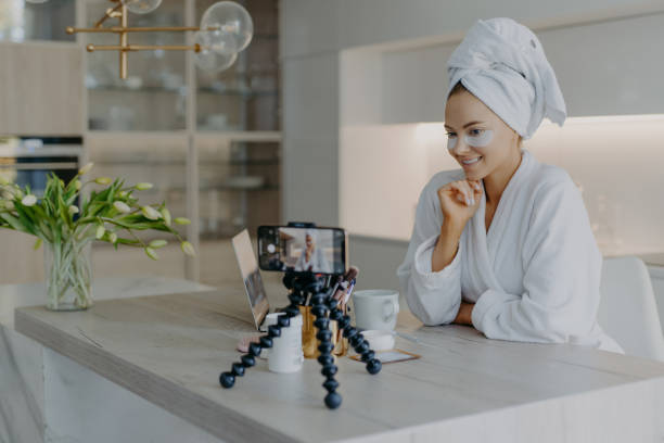 istock Beautiful successful female blogger records tutorial video talks with followers looks at camera of smartphone on tripod applies beauty patches under eyes dicuss how to care about skin and complexion 1415550219