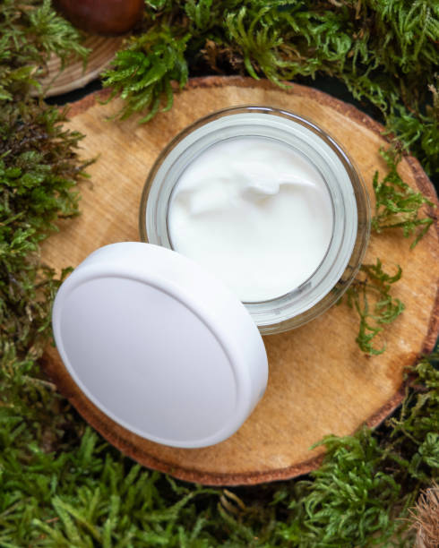 istock Opened cream jar with white cap on wooden piece between green moss, top view, mockup 1415551892