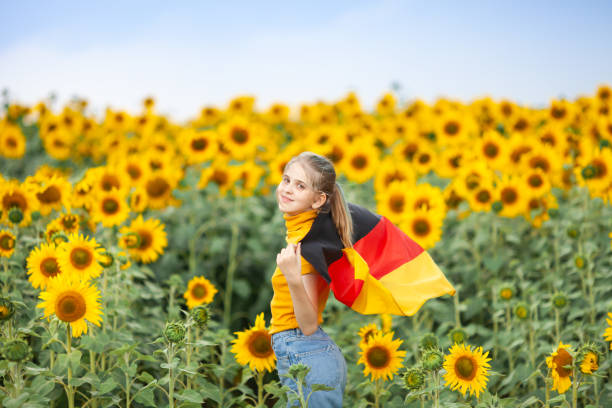 Blond girl holding waving flag of Germany in the sunflower field. stock photo