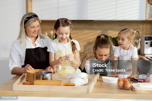 Eldest Daughter Molds Dough Mother Is Looking For Vessel For Baking Grandmother Wathcing Process Preschooler Daughter Managing Process Women Delighted Spending Time In The Kitchen Stock Photo - Download Image Now