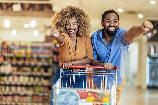 African American couple with trolley purchasing groceries at mall, having fun.