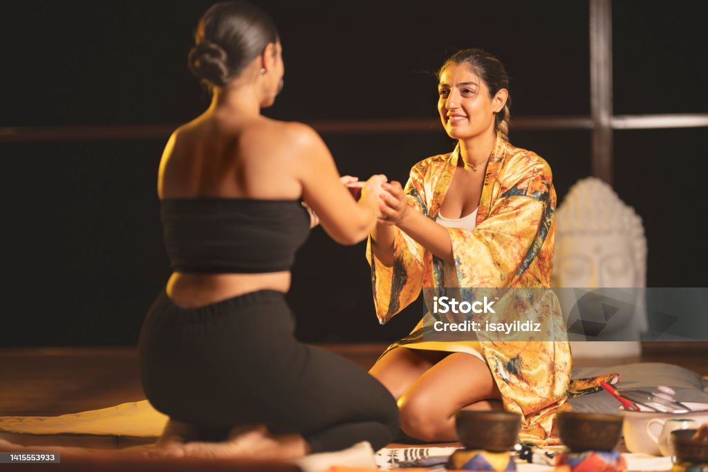 Young woman is having cacao ceremony. Group of Friends Having Cacao Ceremony. Person giving ceremonial cacao in cup. Relaxation and meditation. Sound therapy. Buddhist healing practices. Clearing the space of negative energy. 20-24 Years Stock Photo
