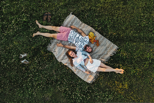 Aerial shot top-down view of middle-aged couple enjoying picnic in the field, caucasian man and woman lying on blanket