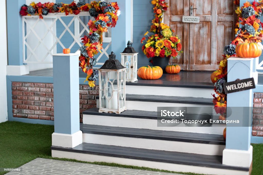 Halloween design home with yellow fall leaves and lanterns. House entrance staircase decorated for autumn holidays, fall flowers and pumpkins. Cozy wooden porch of the house with pumpkins in fall time Halloween Stock Photo