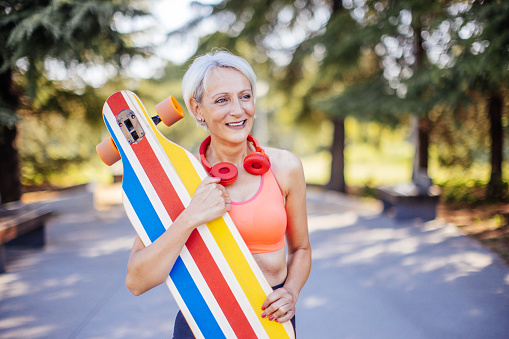 Active senior woman enjoying her free time while skateboarding in park wearing sports clothes and headphones