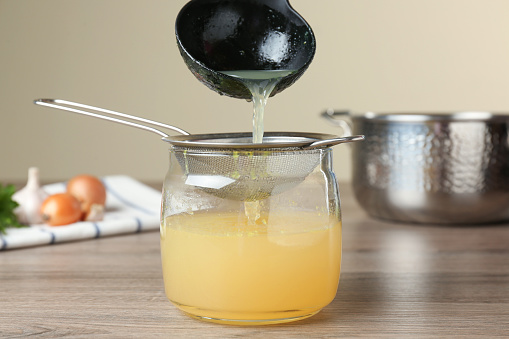 Straining delicious broth through sieve on wooden table