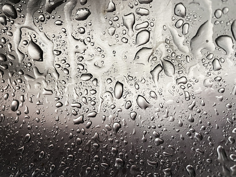 Close-up of water drops falling on transparent glass window.