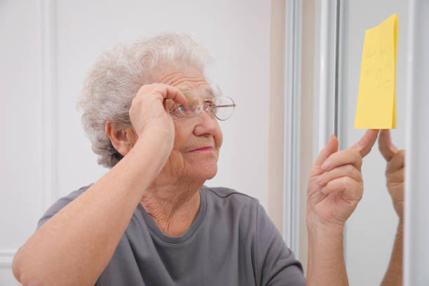 Senior woman looking at reminder note indoors. Age-related memory impairment