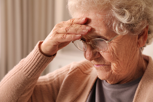 Senior woman with headache at home, closeup. Symptom of age-related memory impairment