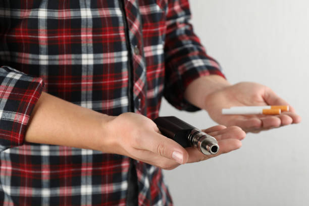 istock Man with cigarettes and vaping device on light background, closeup. Smoking alternative 1415564979