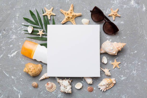 istock Summer time concept with blank greeting card and blank white paper on colored background. Seashells from ocean shore in the shape of frame separated with space for text top view 1415567500