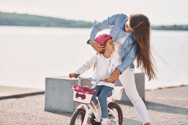 a mulher está ajudando a garotinha. mãe com sua filha mais nova está com bicicleta ao ar livre juntos - pink pants summer two people - fotografias e filmes do acervo