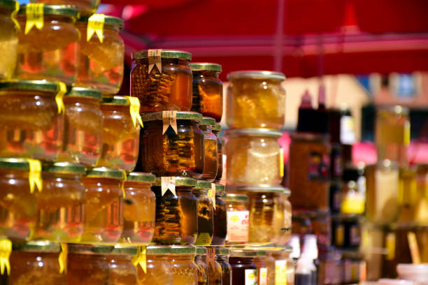 golden color honey jars in bright sunlight on display in open market place. small glass containers with metal lids, shiny and reflective with shadow. food concept. wooden table. organic origin concept