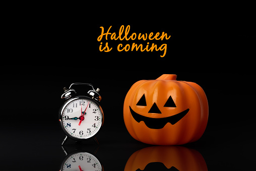 Halloween is coming. Toy pumpkin next to a clock symbolizing the approaching Halloween holiday. Time to dress up as a witch or zombie