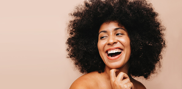 Beautiful woman with an Afro hairstyle laughing happily while standing in a studio. Self-confident woman of color wearing her natural curly hair with pride.