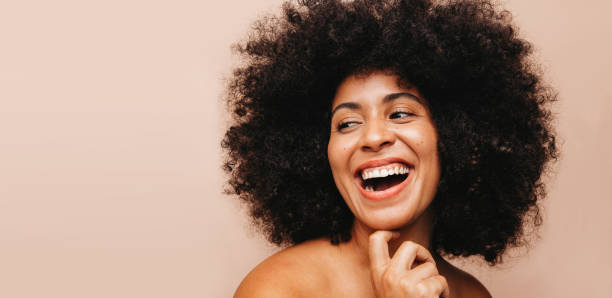 Beautiful woman with Afro hair laughing cheerfully in a studio Beautiful woman with an Afro hairstyle laughing happily while standing in a studio. Self-confident woman of color wearing her natural curly hair with pride. natural hair stock pictures, royalty-free photos & images