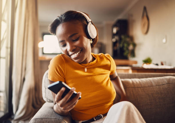 Happy, smiling and carefree young woman texting, browsing and scrolling social media on a phone while listening to music, podcast or watching funny internet memes while relaxing on a sofa at home mujer joven enviando mensajes de texto, navegando y desplazándose por las redes sociales en un teléfono sintiéndose feliz, despreocupada y sonriente. escuchar música, podcast o ver divertidos memes de internet en línea mientras se relaja en un sofá