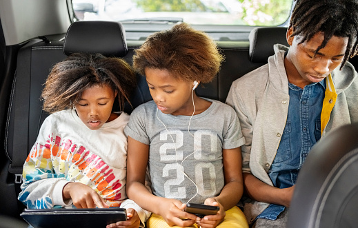 Siblings using digital tablet and smartphone while driving in the backseat of the car
