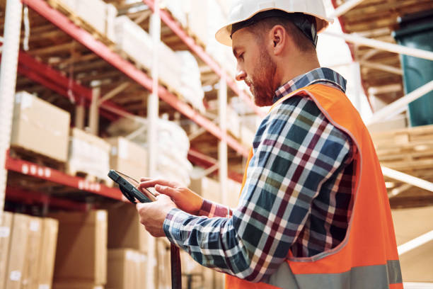 istock Holding tablet in hands. Employee in uniform is working in the storage at daytime 1415574437