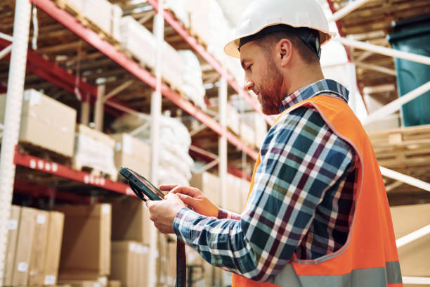 istock Holding tablet in hands. Employee in uniform is working in the storage at daytime 1415574471