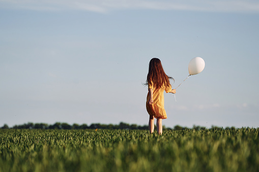 Running with balloon in hand. Happy girl have a walk outdoors on the field at summer.