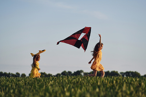 Running with kite. Two girls have fun outdoors on the field at summer.